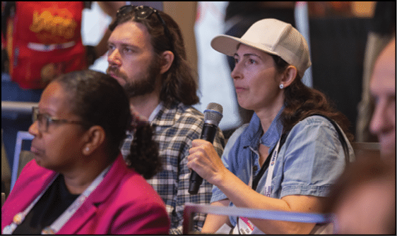 Several adults are seated indoors, with one person holding a microphone and appearing to speak or ask a question. Description generated by AI