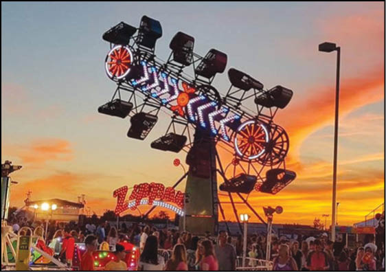 A brightly lit amusement park ride with seats arranged in a circular pattern is spinning above a crowd of people at sunset. Description generated by AI