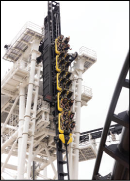 A group of people seated in a yellow roller coaster car is ascending a vertical track structure at an amusement park. Description generated by AI