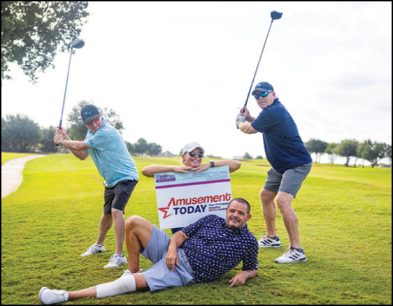 Three adults on a golf course pose playfully with two holding golf clubs ready to swing and one lying on the grass holding a sign that reads Amusement Today. Description generated by AI