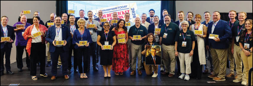 A large group of adults standing on a stage holding plaques and smiling in front of a screen displaying colorful text. Description generated by AI