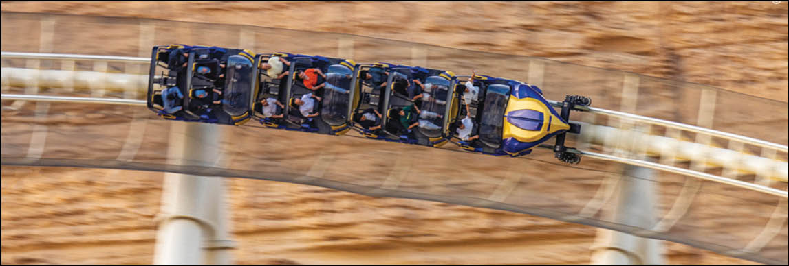 A roller coaster with several people seated is captured in motion on a curved track above a rocky background. Description generated by AI