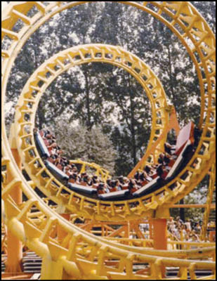 A group of people are riding a yellow roller coaster as it loops through two circular tracks surrounded by trees. Description generated by AI
