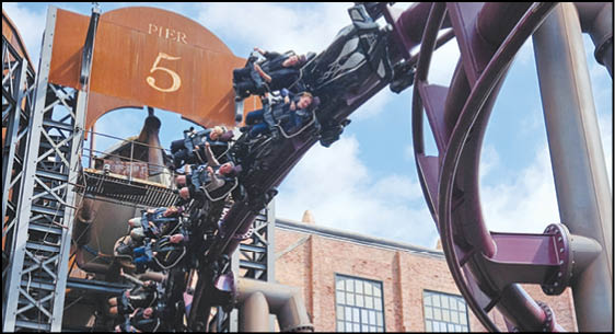 A group of people are riding a roller coaster that is curving sharply near a structure labeled Pier 5 against a partly cloudy sky. Description generated by AI
