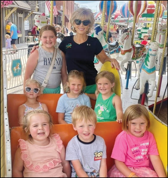 A group of children and one adult are smiling and posing together on a colorful carousel ride at an amusement park. Description generated by AI